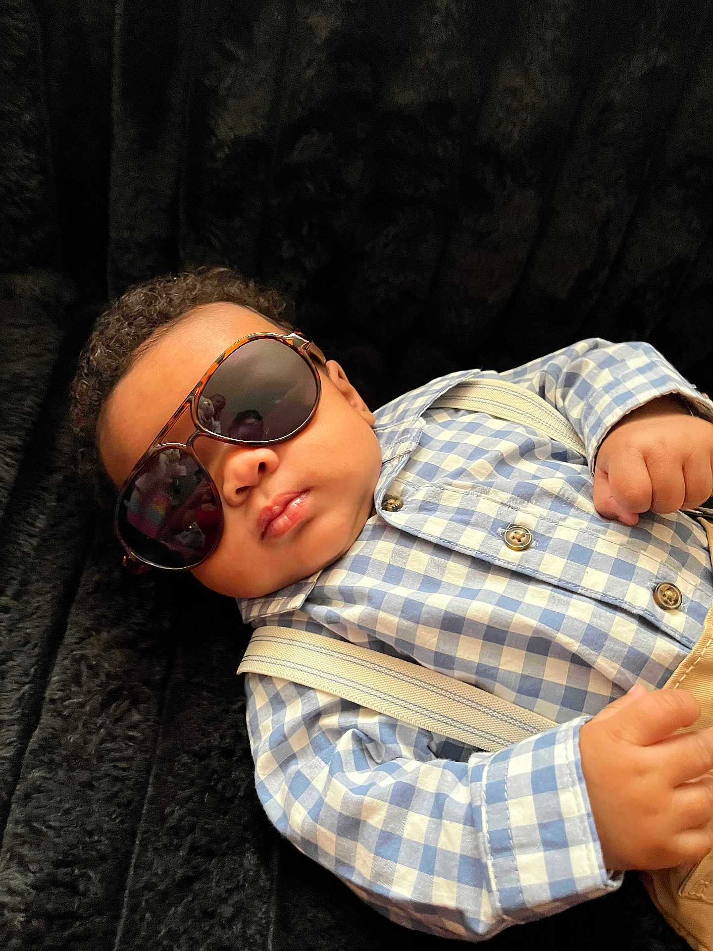 Jai Ceon is registered to the contest to win money with this photo: baby, sunglasses, blue_checkered_shirt, suspenders, plush_surface, curly_hair, infant, portrait, fashion, cool, relaxed, indoor, child, cute, small_hands, accessory, casual, person, closeup, resting