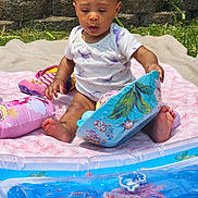 Amaya joined the competition — help win amazing prizes! baby, blanket, book, child, colorful, cute, expression, face, grass, inflatable, nature, outdoor, playing, portrait, sitting, summer, sunlight, toy, water, young