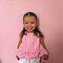 child, girl, smiling, happy, pink_wall, pink_top, white_shorts, bracelet, dimples, portrait, standing, indoor, cute, fashion, hair, young, childhood, person, casual, colorful