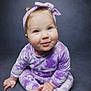 baby, barefoot, blue_eyes, child, chubby_cheeks, closeup, cute, foot, gray_background, hand, headband, infant, onesie, portrait, purple_outfit, sitting, smile, soft_lighting, studio_background, tie_dye