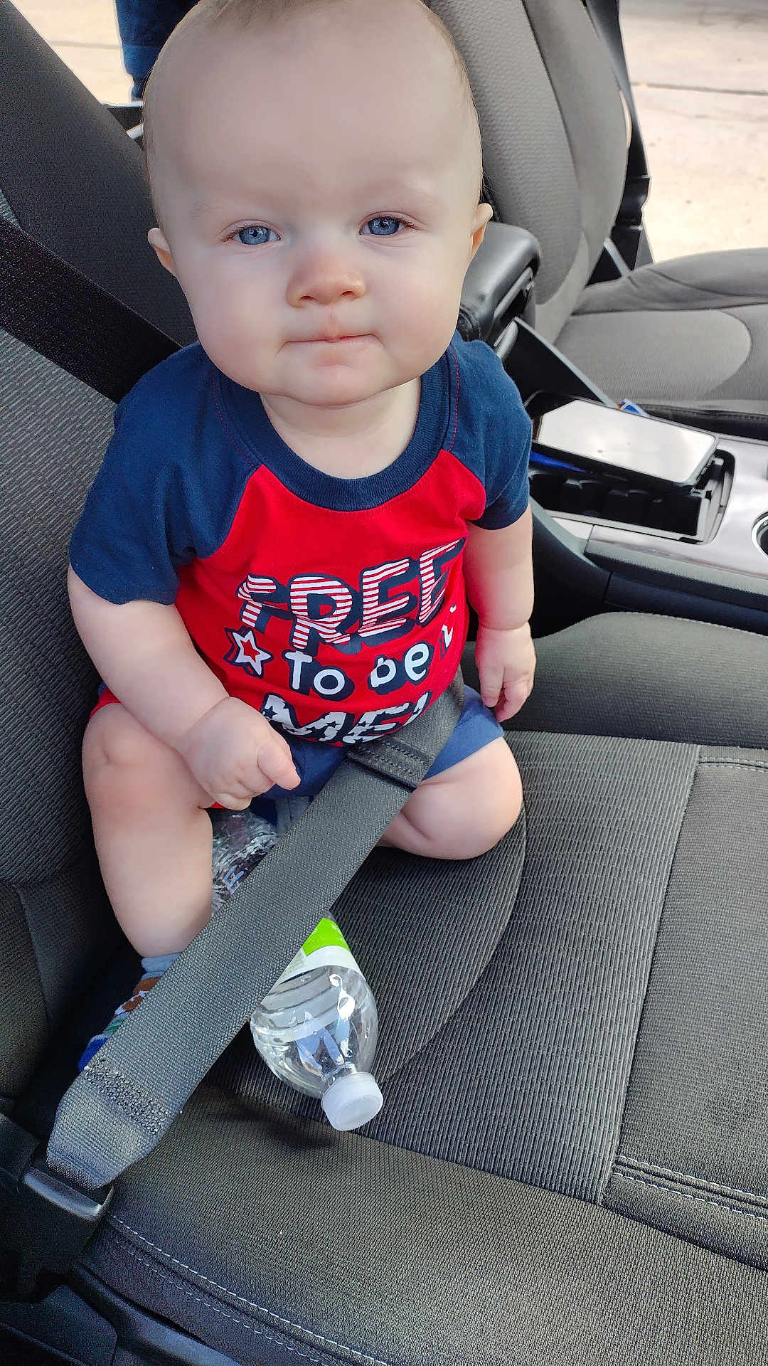 Tristan is registered to the contest to win money with this photo: baby, child, car_seat, seatbelt, water_bottle, blue_eyes, red_shirt, shorts, car_interior, seat, sitting, clothing, person, infant, cute, portrait, vehicle, safety, expression, indoors