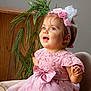 toddler, child, pink_dress, headband, bow, blue_eyes, smiling, happy, sitting, chair, wooden_background, green_plant, flowers, portrait, indoor, cute, baby, lace, person, fashion