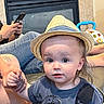 toddler, child, hat, straw_hat, dinosaur_tshirt, hand_holding, person, adult, tattoo, jeans, phone, toy, indoor, fireplace, curious, baby_toy, casual, seated, portrait, cute