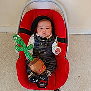 Zakariya a rejoint le concours — aidez-le/la à gagner de superbes lots ! baby, cactus_toy, carpet, child, clothing, cute, expression, face, footwear, head, indoor, infant, looking_at_camera, person, pinstripe_suit, plush_toy, red_baby_carrier, seated, small_hands, wall