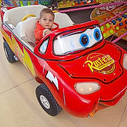 Solan a rejoint le concours — aidez-le/la à gagner de superbes lots ! amusement_park, cartoon, child, clothing, colorful, daytime, entertainment, family, fun, jacket, leisure, outdoor, person, playful, red_car, ride, serious_expression, toddler, toy_car, wheels