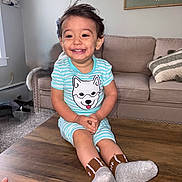 Azariell joined the competition — help win amazing prizes! carpet, child, couch, cute, dog_print, furniture, hands, happy, indoor, living_room, person, pillow, sitting, smiling, socks, striped_clothing, table, toddler, wall_art, wood