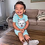 carpet, child, couch, cute, dog_print, furniture, hands, happy, indoor, living_room, person, pillow, sitting, smiling, socks, striped_clothing, table, toddler, wall_art, wood