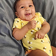 Trinity is registered to the contest to win money with this photo: baby, child, smiling, yellow_onesie, bee_pattern, infant, cushion, gray_fabric, happy, cute, portrait, indoors, relaxed, skin, hand, face, head, person, young, comfortable