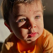 Frank is registered to the contest to win money with this photo: toddler, child, portrait, close_up, face, eyes, hair, orange_clothing, expression, innocence, sunlight, soft_light, indoors, curious, cute, young_child, skin, person, baby, head