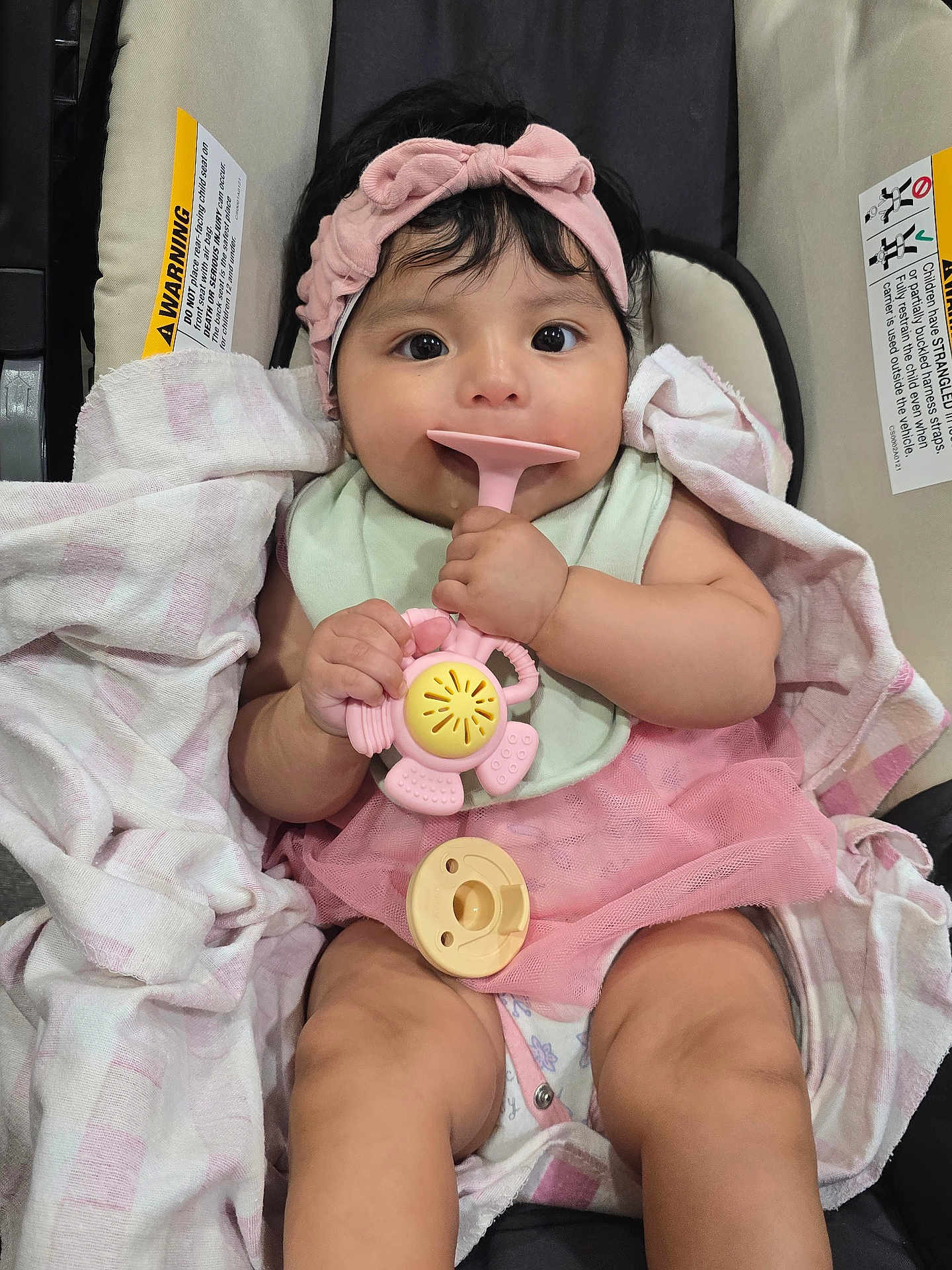 Arleth is registered to the contest to win money with this photo: baby, infant, car_seat, pink_headband, pink_tutu, toy, pacifier, blanket, clothing, hand, face, person, cute, sitting, indoors, child, expression, cute_outfit, soft_toy, closeup