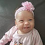 baby, infant, smile, headband, flower, pink_clothing, pink_headband, tongue_out, cute, portrait, child, person, indoors, soft_background, face, young_child, happy, baby_girl, headshot, closeup