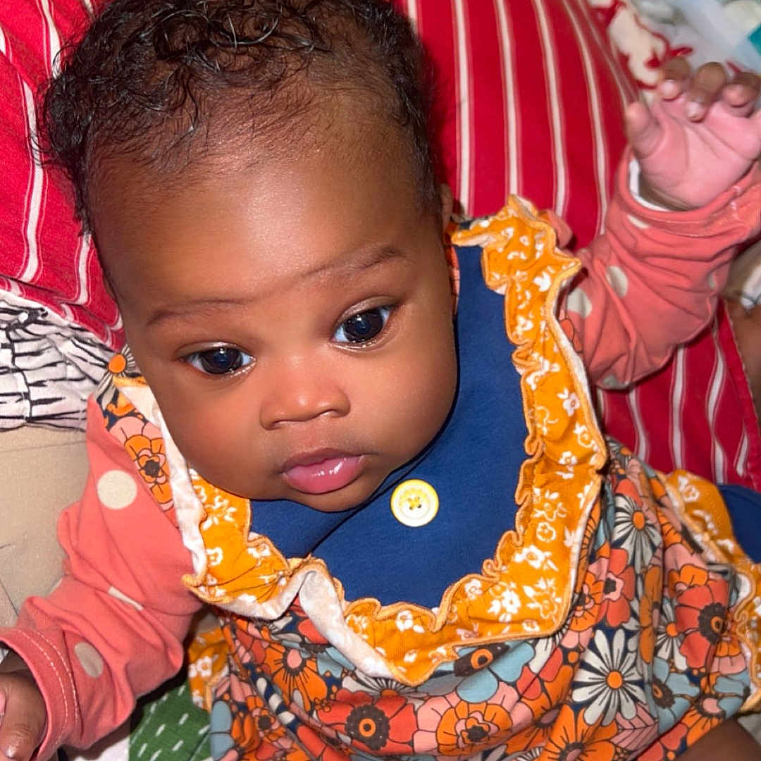 Kehlani joined the competition — help win amazing prizes! baby, blanket, blue, child, clothing, cute, eyes, face, floral_pattern, hands, indoor, infant, orange, person, pillow, portrait, sitting, skin, socks, young