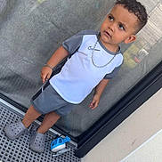 Swaïn a rejoint le concours — aidez-le/la à gagner de superbes lots ! toddler, child, boy, curly_hair, gray_clothing, crocs, chain_necklace, toy_helicopter, glass_door, outdoor, concrete_floor, trash_bag, bottle, side_view, casual, shorts, short_sleeves, standing, expression, reflection