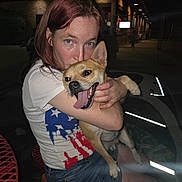 Jake. is registered to the contest to win money with this photo: american_flag_shirt, animal, bench, casual_clothing, dark_background, dog, face, happy, hugging, joy, light, nighttime, outdoor, person, pet, red_hair, shorts, smiling, tongue_out, woman