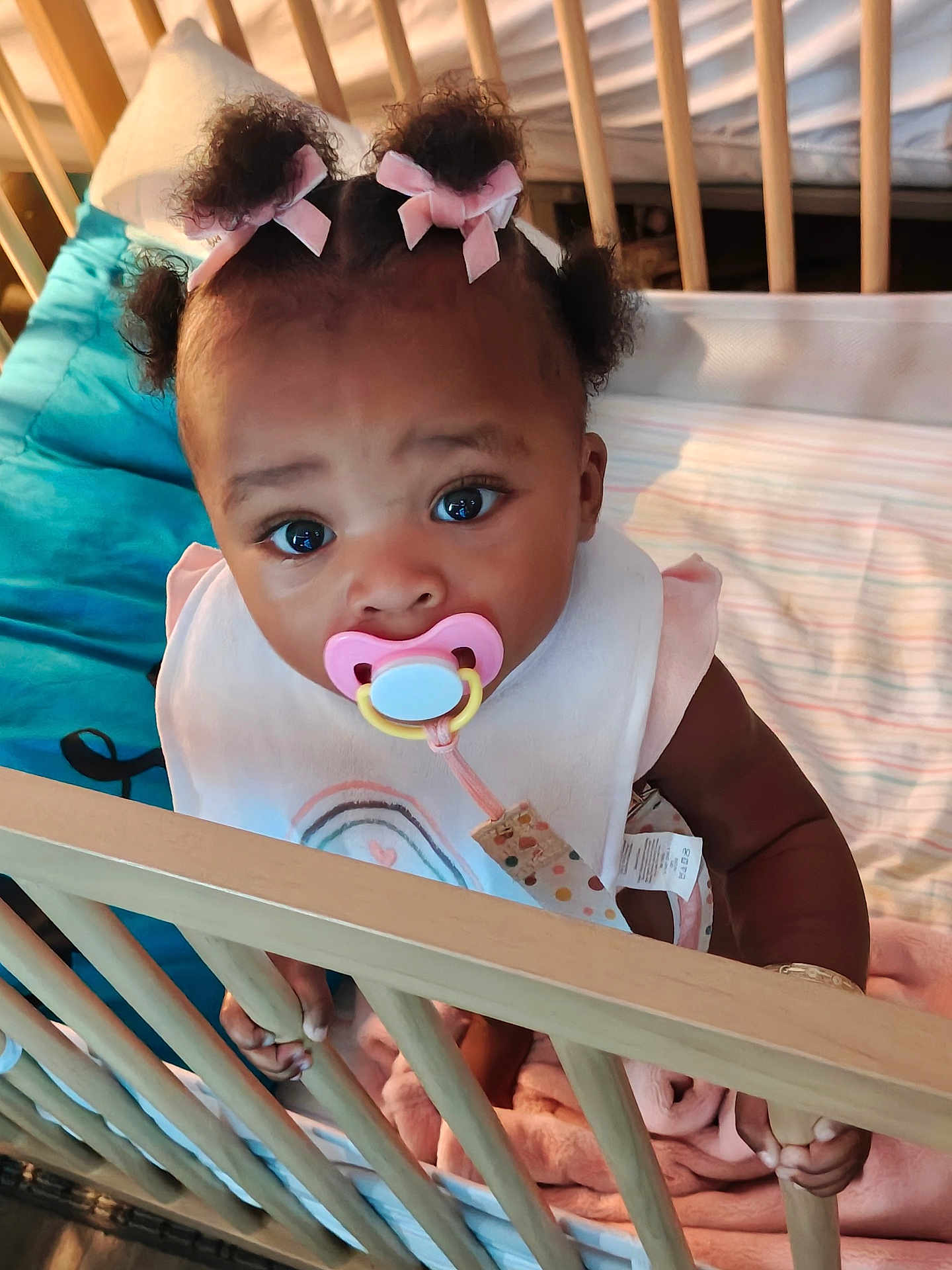 Cherish is registered to the contest to win money with this photo: baby, pacifier, crib, bows, blanket, infant, child, cute, indoors, sleeping_area, clothing, hand, portrait, person, baby_girl, bed, soft_toys, colorful, closeup, curious