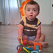 Colton is registered to the contest to win money with this photo: baby, backpack, blue, child, clothing, curtains, cute, expression, floor, hand, indoor, octopus_toy, orange, person, playful, sitting, toy, wide_eyes, wooden_floor, yellow