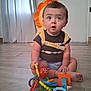 baby, backpack, blue, child, clothing, curtains, cute, expression, floor, hand, indoor, octopus_toy, orange, person, playful, sitting, toy, wide_eyes, wooden_floor, yellow