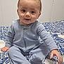 Colton is registered to the contest to win money with this photo: baby, bedspread, blue_onesie, child, cozy, cute, eyes, face, footed_pajamas, hair, hand, home, indoor, infant, mohaawk, patterned_bedspread, person, sitting, smiling, young_child