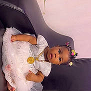 Aurora joined the competition — help win amazing prizes! adorable, baby, black_couch, child, couch, cute, decor, dress, flowers, furniture, gold_chain, hair_clips, indoor, infant, lace, portrait, sitting, skin, white_dress, young_child