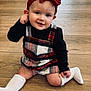 baby, child, headband, red_bow, plaid_dress, black_shirt, white_socks, wooden_floor, smile, sitting, cute, indoors, person, infant, young_child, playful, fashion, portrait, happy, cozy