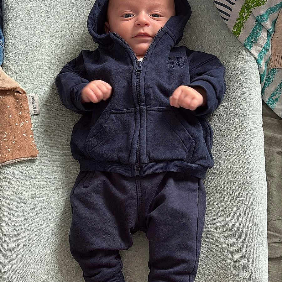 Isaïe a rejoint le concours — aidez-le/la à gagner de superbes lots ! baby, bed, blanket, casual, changing_pad, clothing, cute, face, hoodie, indoor, infant, lying_down, neutral_expression, newborn, pants, person, resting, socks, soft_texture, young_child