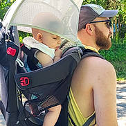 Mason joined the competition — help win amazing prizes! baby, backpack, beard, carrier, casual_clothing, child, footwear, greenery, headwear, man, nature, outdoor, park, person, shade, summer, sunglasses, sunlight, trees, walking