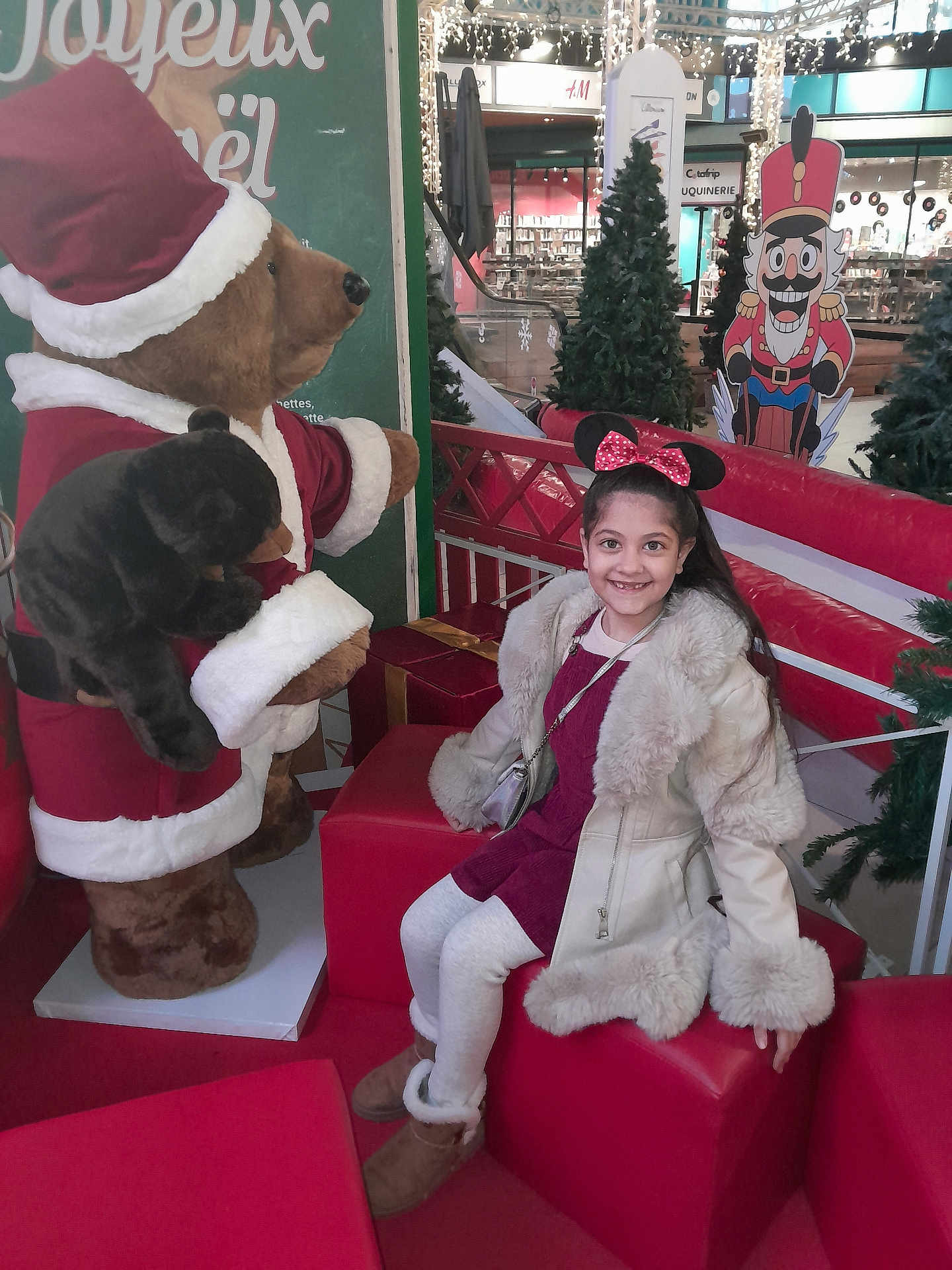 Andra Maria a rejoint le concours — aidez-le/la à gagner de superbes lots ! child, girl, smiling, coat, minnie_mouse_ears, red_dress, white_tights, boots, stuffed_bear, santa_costume, christmas_decorations, gift_box, shopping_mall, festive, holiday, decorative_trees, bench, red_cushion, nutcracker, indoor