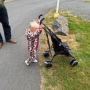 Brynnlee is registered to the contest to win money with this photo: child, toddler, stroller, pavement, grass, rock, adult, boots, jacket, outdoor, park, rv, picnic_table, vehicle, toy, walking, playing, daytime, casual, nature
