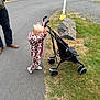 child, toddler, stroller, pavement, grass, rock, adult, boots, jacket, outdoor, park, rv, picnic_table, vehicle, toy, walking, playing, daytime, casual, nature