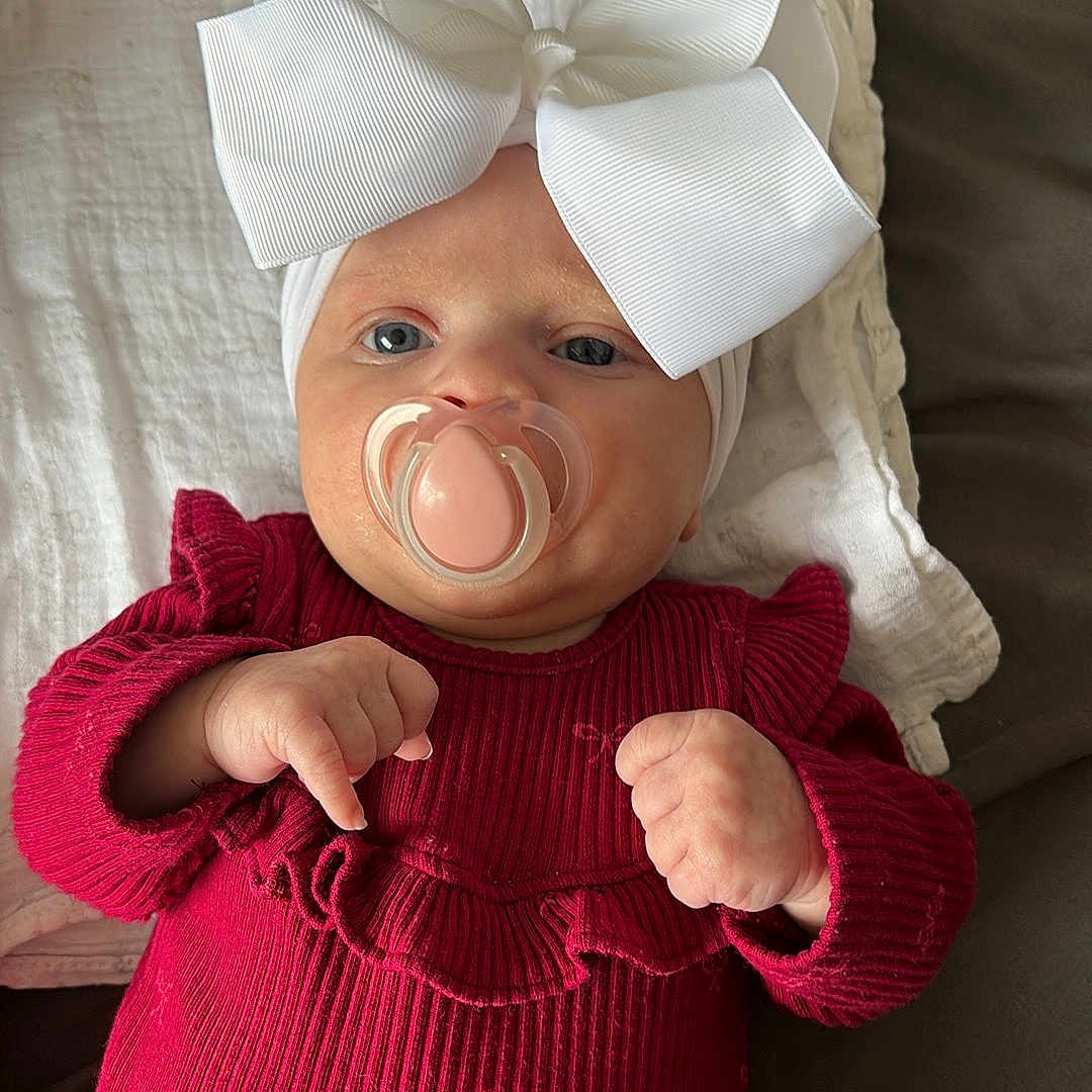 Isabella is registered to the contest to win money with this photo: baby, blanket, bow, child, cozy, cute, face, hands, headband, indoors, infant, lying_down, newborn, pacifier, portrait, red_clothing, skin, sleepy, small_hands, soft_texture