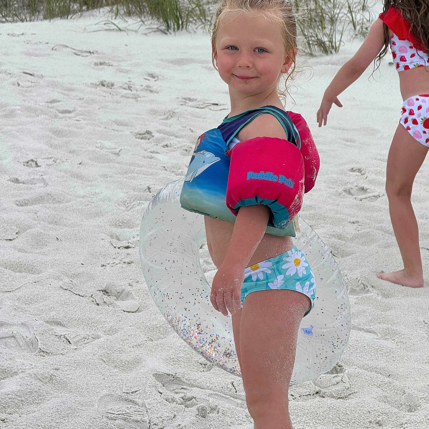 Ava is registered to the contest to win money with this photo: barefoot, beach, casual, child, floaties, footprints, fun, girl, grass, happy, inflatable_ring, outdoor, playful, sand, smiling, summer, sunny, swimsuit, vacation, water_toys