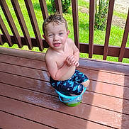 Gunner joined the competition — help win amazing prizes! child, boy, bucket, wet_hair, smiling, outdoor, deck, wooden_floor, sunlight, greenery, playful, summer, bare_chest, shorts, grass, railing, happy, sitting, water, daylight