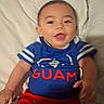 baby, child, infant, smiling, happy, portrait, indoors, bed, pillow, blue_shirt, red_pants, clothing, sitting, lying_down, face, eyes, mouth, hands, bedroom, guam