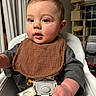 baby, child, high_chair, infant, bib, sitting, indoors, portrait, face, eyes, brown_bib, gray_clothing, happy, curious, open_mouth, short_hair, home, curtains, cat_tree, window