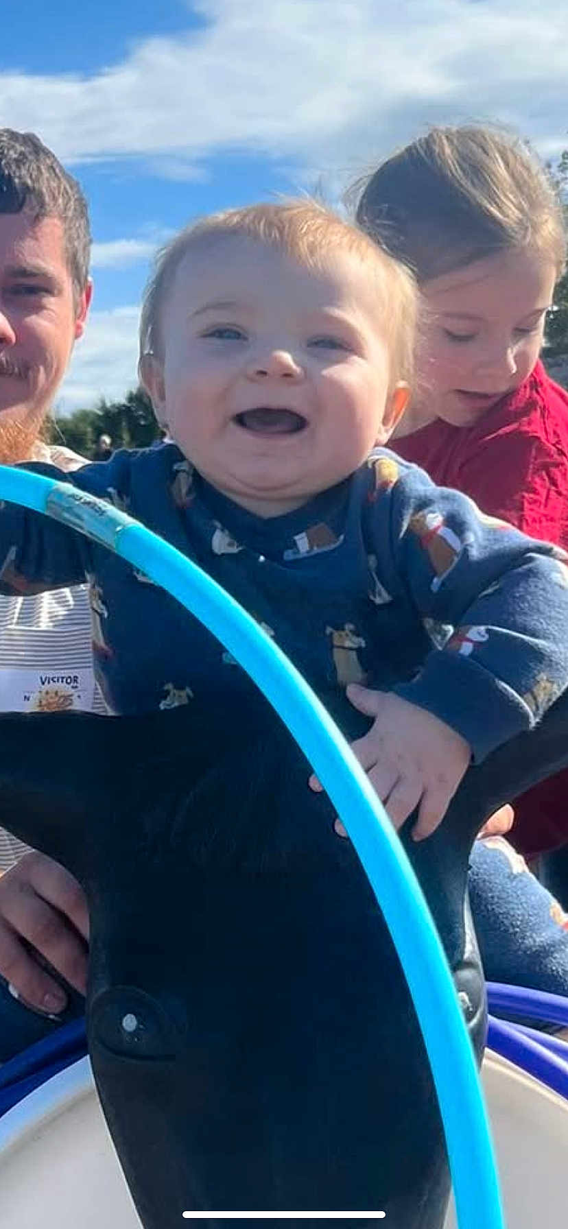 River is registered to the contest to win money with this photo: toddler, child, girl, man, dolphin, playground, outdoor, sky, blue_sky, smile, happy, toy, play, daylight, person, clothing, family, fun, nature, park