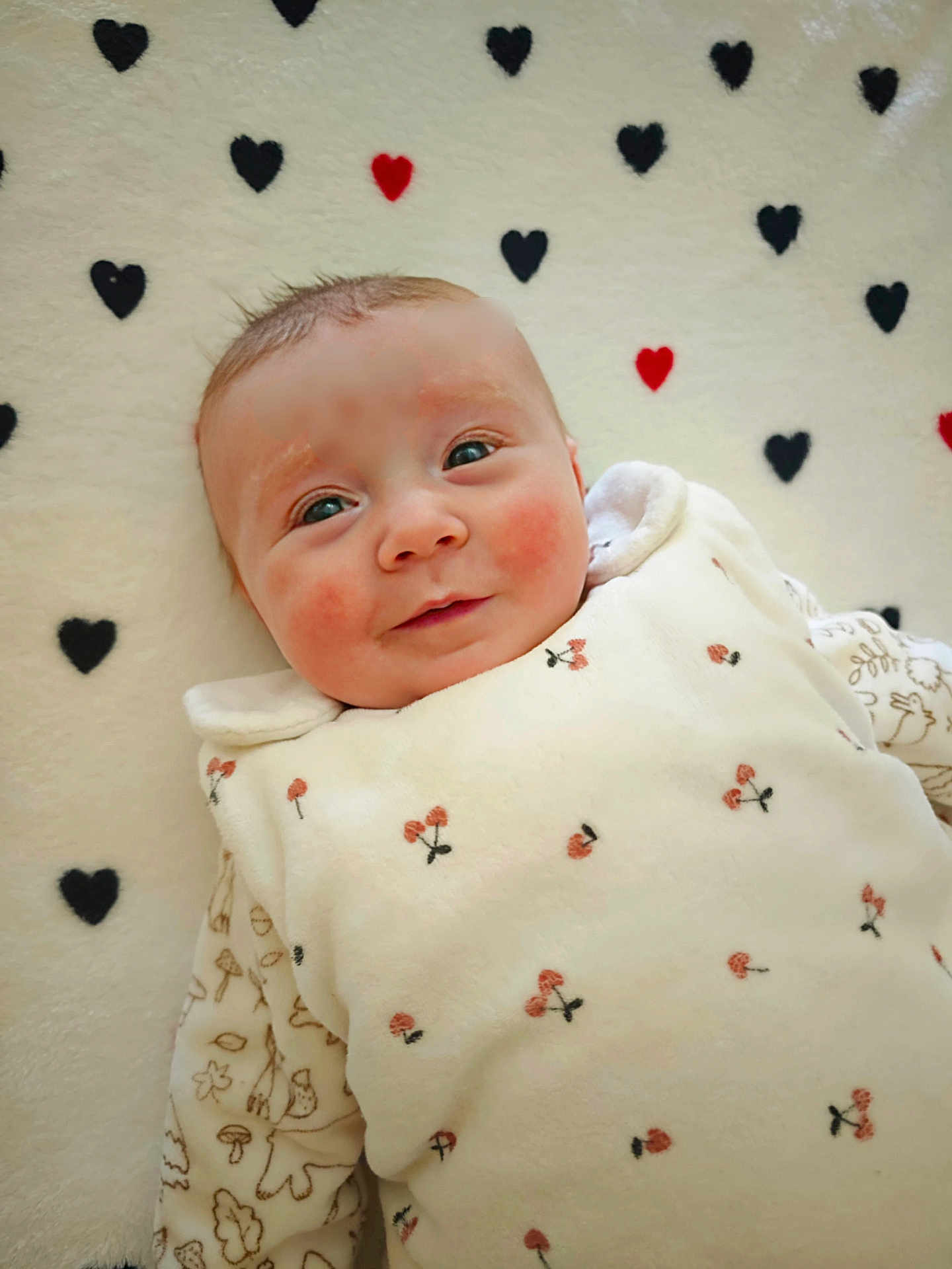 Effy a rejoint le concours — aidez-le/la à gagner de superbes lots ! baby, infant, smile, face, rosy_cheeks, blanket, heart_pattern, white_clothing, cherry_pattern, lying_down, cute, soft_texture, indoors, portrait, child, newborn, cozy, warm, happy, person