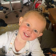 Syanna participe au concours pour gagner de l'argent avec cette photo : apron, blond_hair, casual, chair, child, clothing, face, floor, furniture, hair_tie, happy, indoor, person, room, shelf, shoes, smiling, table, toddler, toy