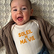 Elio a rejoint le concours — aidez-le/la à gagner de superbes lots ! baby, infant, smiling, happy, face, clothing, cardigan, denim, jeans, text, blanket, pattern, ribbed, casual, portrait, cute, child, young, closeup, indoor