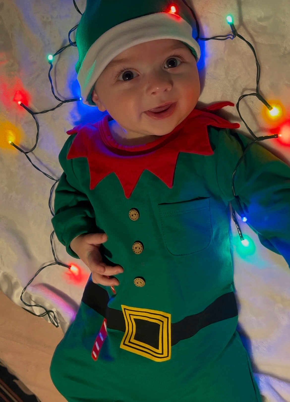 Oden joined the competition — help win amazing prizes! baby, child, elf_costume, christmas_lights, holiday, festive, smiling, tongue_out, cute, green_clothing, red_collar, hat, buttons, belt, sleeping_bag, indoor, portrait, face, holiday_cheer, bright_colors