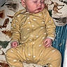 baby, sleeping, onesie, yellow_clothing, infant, cushion, animal_print, deer, pine_tree, bedtime, sleepwear, child, indoors, peaceful, resting, face, hand, footed_pajamas, blanket, comfort