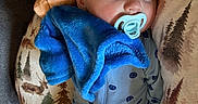 Jaxsyn is registered to the contest to win money with this photo: baby, sleeping, pacifier, blue_pajamas, plush_blanket, couch, pillow, nature_pattern, cozy, infant, child, smile_pattern, resting, indoors, soft_texture, comfort, peaceful, head, face, person