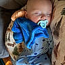 baby, sleeping, pacifier, blue_pajamas, plush_blanket, couch, pillow, nature_pattern, cozy, infant, child, smile_pattern, resting, indoors, soft_texture, comfort, peaceful, head, face, person