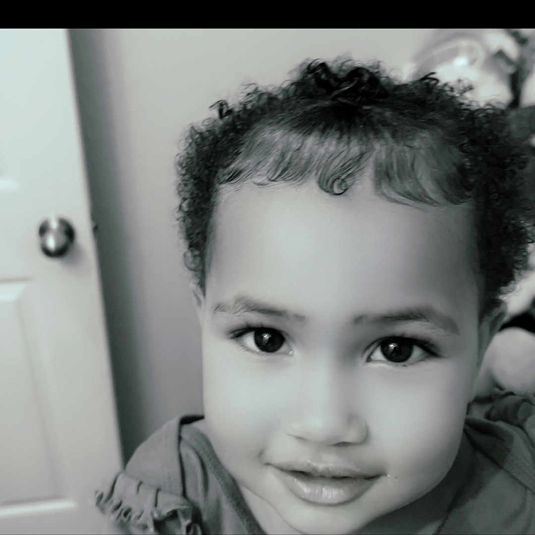 Ruby is registered to the contest to win money with this photo: baby, black_and_white, child, childhood, close_up, curly_hair, cute, expression, eyes, face, hair, happy, headshot, indoors, innocence, person, portrait, smile, toddler, young_child