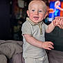 baby, child, smiling, standing, hand_holding, indoor, bed, clothing, shorts, polo_shirt, blue_eyes, cheerful, person, portrait, cute, infant, home, blurred_background, happy, young
