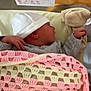newborn, baby, sleeping, hat, blanket, crochet, crib, pacifier, hospital, clothing, infant, hand, face, side_profile, resting, cozy, soft, pink, cream, gray