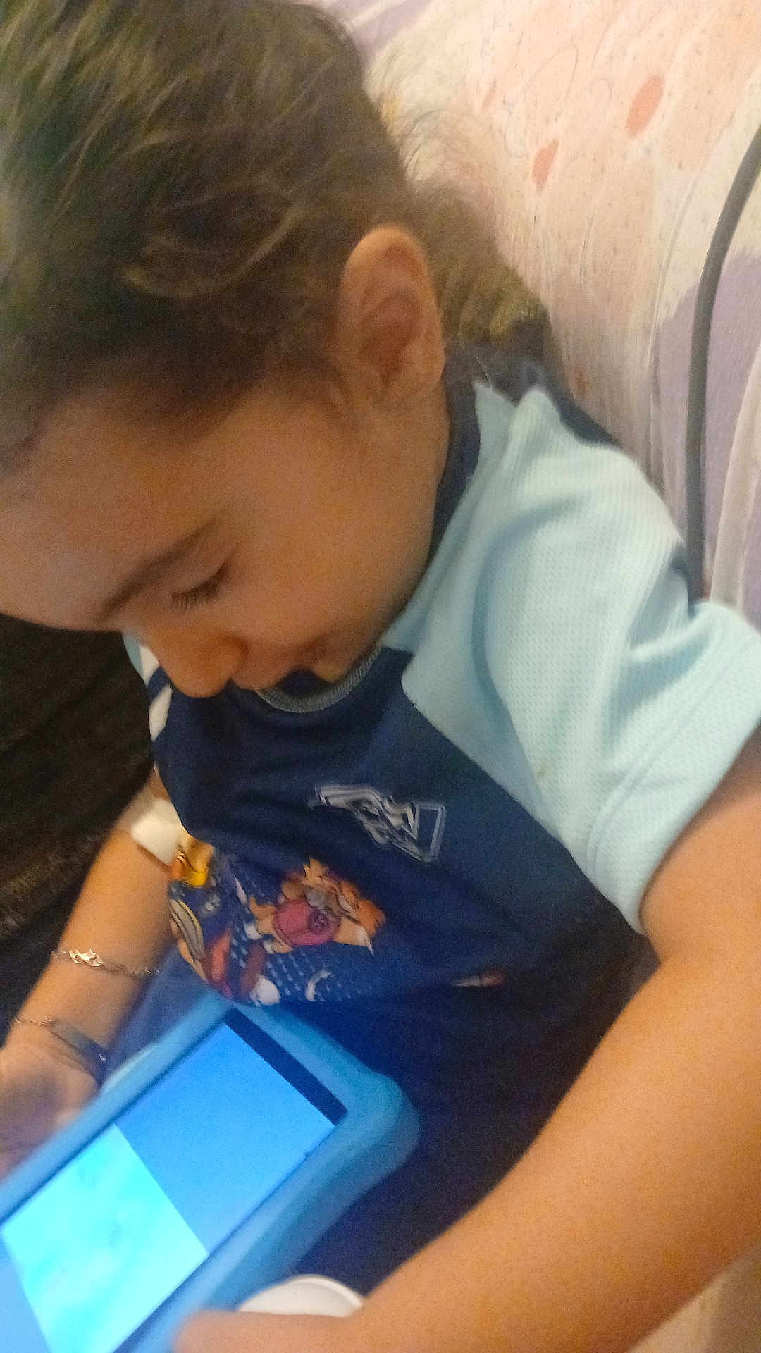 Jayden a rejoint le concours — aidez-le/la à gagner de superbes lots ! child, curly_hair, tablet, blue_case, sitting, couch, arm, bracelet, clothing, patterned_fabric, indoor, technology, screen, person, casual, focused, young, device, relaxing, home