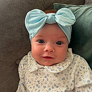 Clodagh joined the competition — help win amazing prizes! baby, child, infant, headband, bow, smile, face, eyes, couch, pillow, clothing, pattern, floral, sitting, indoors, portrait, cute, young, soft_lighting, happy