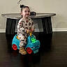 child, toddler, toy_car, indoor, floor, table, wooden_floor, smiling, cute, playful, pony_tail, boots, pajamas, colorful, glowing_eyes, furniture, person, happy, young_child, home