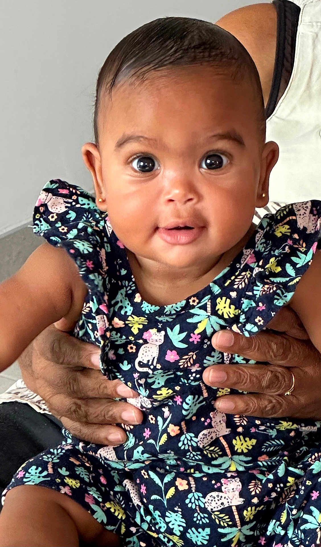 Kelane a rejoint le concours — aidez-le/la à gagner de superbes lots ! baby, child, infant, person, hands, clothing, patterned_dress, floral_pattern, animal_print, cute, wide_eyes, expression, holding, adult_hands, skin, portrait, indoor, closeup, face, earrings