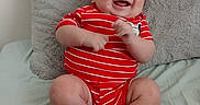 Ares is registered to the contest to win money with this photo: baby, bed, child, chubby_legs, cute, face, happy, indoor, infant, joyful, person, pillow, playful, plush_pillow, red_onesie, sitting, smiling, soft_texture, striped_clothing, white_socks